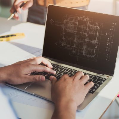 Two professional architects discussing house building plan design project with looking blueprints in computer at desk in office.